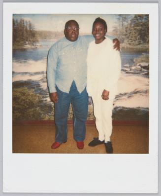 [Man wearing glasses and button up shirt with arm around woman in white pants and top]