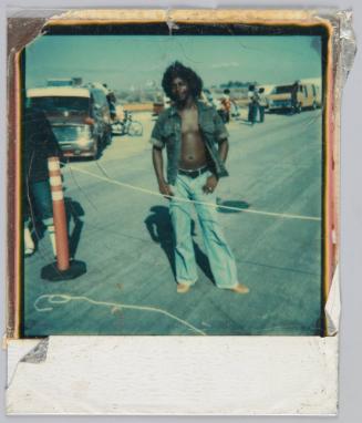 [Man with shirt unbottoned and afro standing in parking lot]