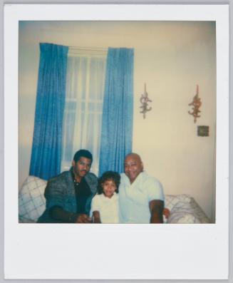 [Girl sitting on couch in between two men, man on left wears tweed blazer]