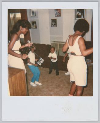 [Two women dancing with young children in carpeted room]