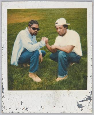 [Two men squatting on the grass while firmly grasping each other's hand]