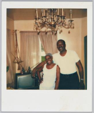 [Man in white tshirt and moustache standing with arm around smiling woman in white tank top]