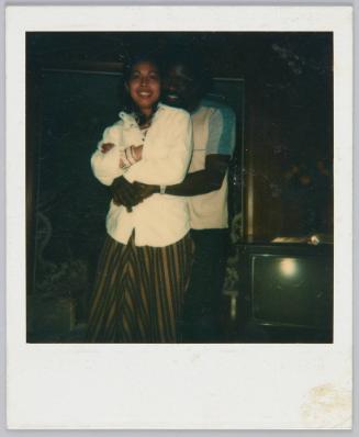 [Couple posing, man standing behind woman with his arms around her]