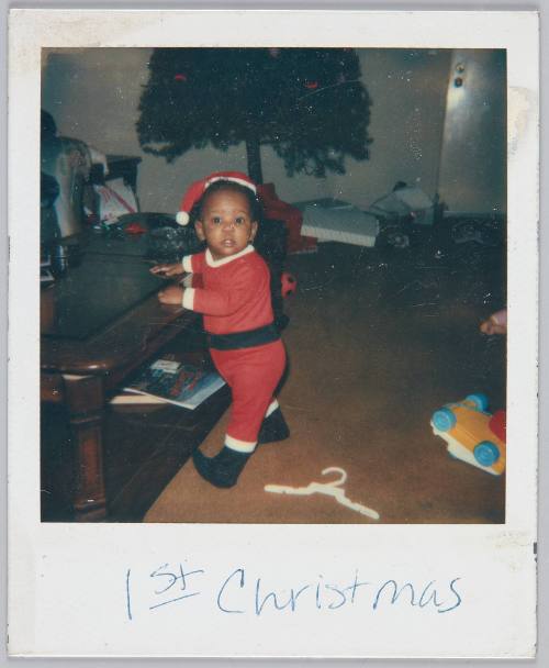 1st Christmas [Baby in santa onesie standing by coffee table]
