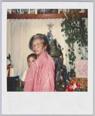 Mode, 12-25-89 [elderly woman in pink jacket and glasses with Christmas tree in background]
