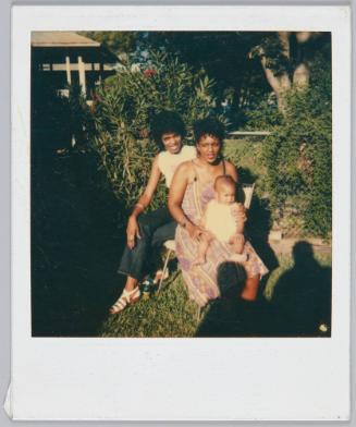 8-26-84 [Two women sharing patio chair, woman in dress holds baby on her lap]