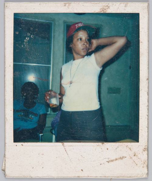 [Woman wearing red hat and white top with one arm stretched behind her head]