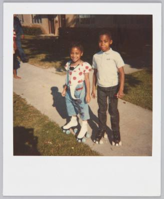 [Little boy and girl wearing rollerskates on sidewalk]