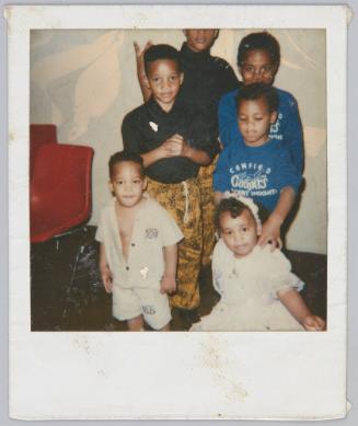 [Group of six children standing around, toddler boy on the left has shirt unbuttoned]