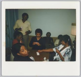 [Group sitting around table playing a game of cards]