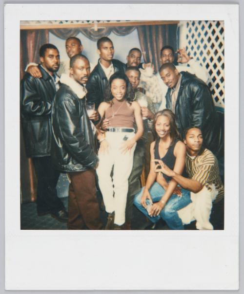 [Stylish group posing, woman in front wearing white pants and brown mock neck tank]