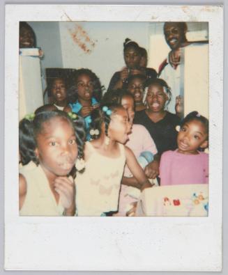 [Eight girls standing in group wearing colourful hair accessories, adults smiling in background]