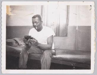 Bon temps -62- to [illeg.] with love [illeg.] [Man sitting on couch wearing a white t-shirt with cigarette hanging from his mouth looking inside a handheld container]