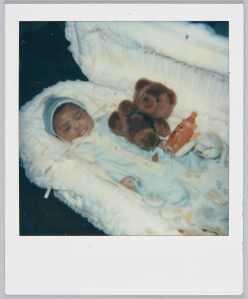 [Baby sleeping in basinet with bottle and brown teddy bear]
