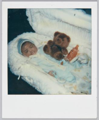 [Baby sleeping in basinet with bottle and brown teddy bear]
