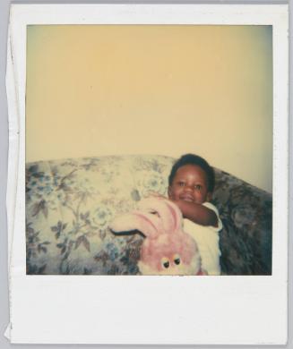 [Child sitting on floral couch holding a pink toy bunny]