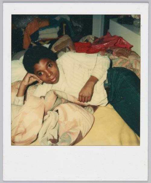 [Boy laying on his side on bed propping his head up with his arm, red plastic bag behind him]