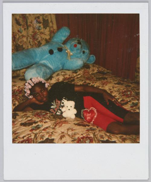 [Girl with pink curlers in her hair, laying on her side in bed with two teddy bears]