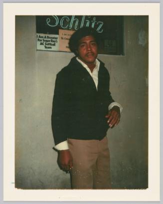 [Man in black sweater standing in front of sign, "Schlitz"]