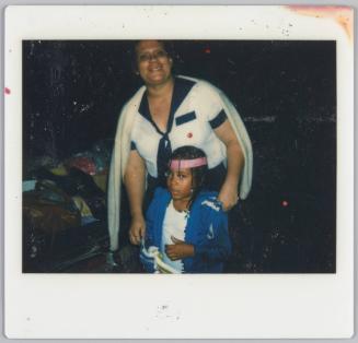[Woman with cardigan set over her shoulders standing with little girl wearing pink headband]
