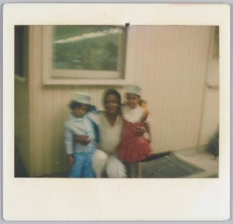 [Blurry image of woman holding two young girls in white hats on either side of her]
