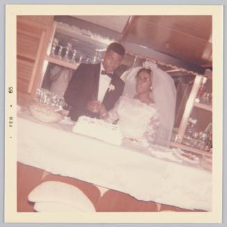 [Bride and groom cutting cake at table, bride is wearing a large veil]

