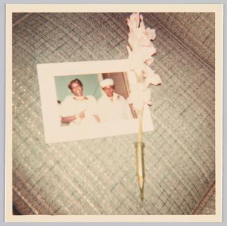[Photograph set on top of upolstered furnitute along with a flower]
