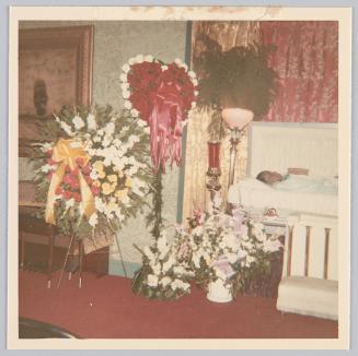 [Open casket funeral, floral arrangements next to coffin]
