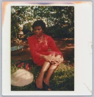 [Woman wearing red dress sitting and holding her knees on grass]
