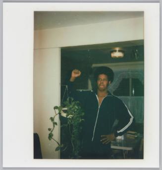 [Man standing in doorway next to hanging planter with one fist raised in the air]
