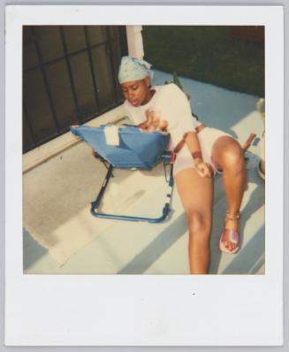 [Woman wearing head scarf sitting on ground with baby in seat]
