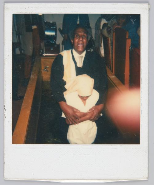 [Priest and child in tub for baptism]
