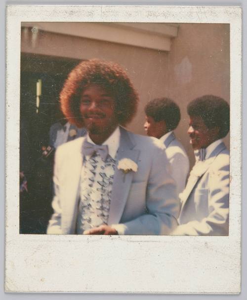 [Young man with curly red-coloured hair smiling and wearing a purple suit]
