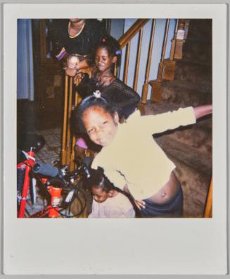 [Girl in white shirt hanging off staircase railing, two more girls on staircase, red bike to the left]