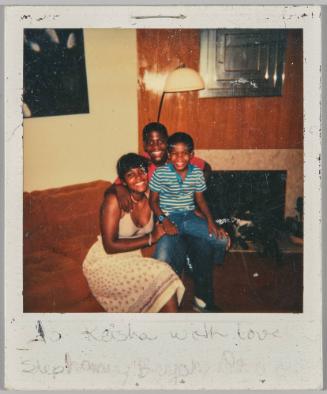 To Keisha with love Stephanie, Bryan, D[illeg.] [Woman sitting on couch, boy sitting on arm of couch, and young man, posed together in front of fireplace]