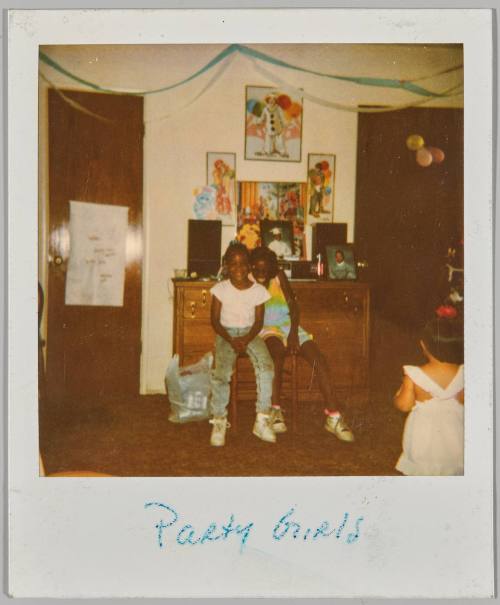 Party Girls [Two girls sitting together and the back of a young girl on the right, steeamers and clown posters on the wall]