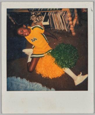 [Girl posing on the floor in yellow and blue cheerleader outfit and pom poms]