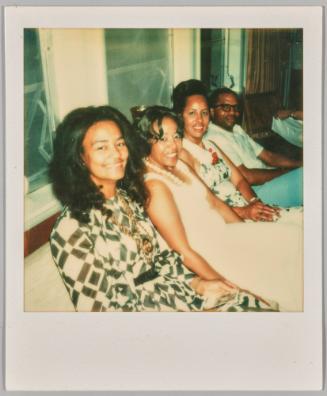 [Three woman and a man sitting together, the woman closest to the camera is in a white and green dress]