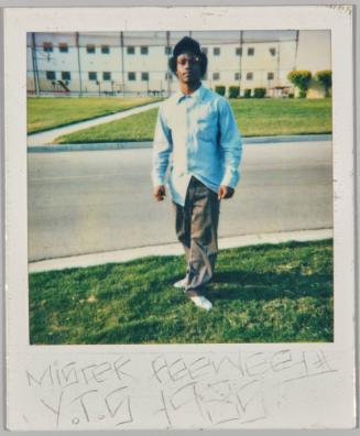 Mister Peewee # Y.T.S 1985 [Young man in black hat and blue shirt standing on grass by curb]