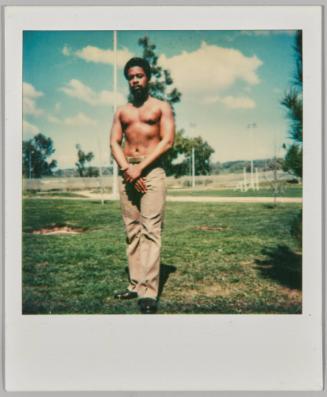 [Shirtless man in brown pants standing with hands together in a park during the day]