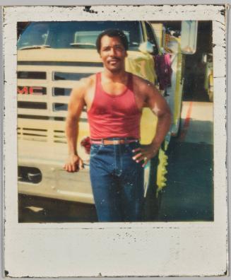 [Man in red tank top and brown leather belt standing in front of GMC truck]