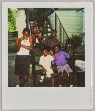 [Five boys posing on black metal staircase outside, boy in centre front giving "Peace" sign]