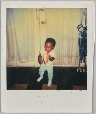 [Toddler standing and holding bag of snacks, folded stroller on the right]