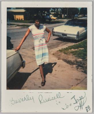 Beverly Russell in [illeg.] Iowa 83 [Woman in dress with drawstring waist leaning on car outside]