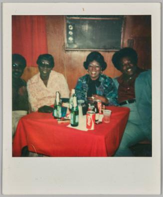 [Four adults sitting at red table with green bottles and cans of Coca Cola]