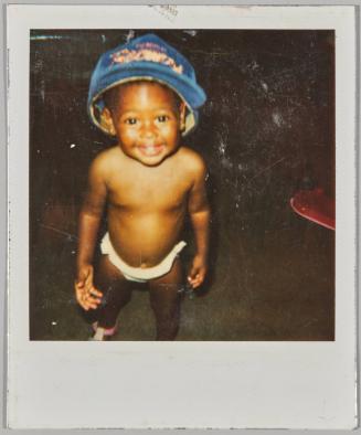 [Toddler in diaper and oversized blue baseball cap, smiling at camera]
