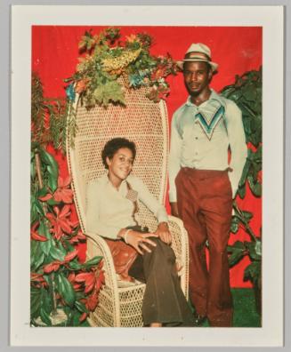 [Man and woman posing in wicker chair with red and white flowers decorating the scene]