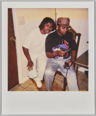 [Woman in white outfit crouching with arm around man sitting in chair]