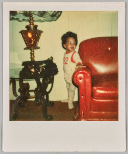 [Toddler standing in between coffee table and red couch]