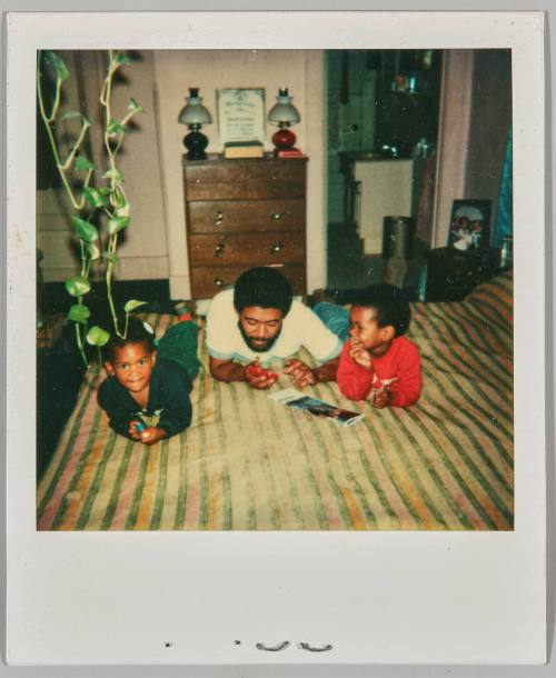 [Man laying on his stomach in between toddler boy and girl on bed]